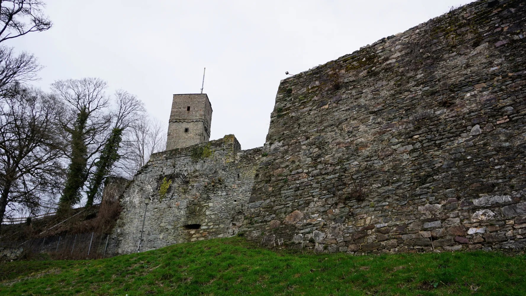 20230319_Deutschland_Hessen_3-Burgen-Weg (4) Ancient stone fortress walls and a square tower under an overcast sky.