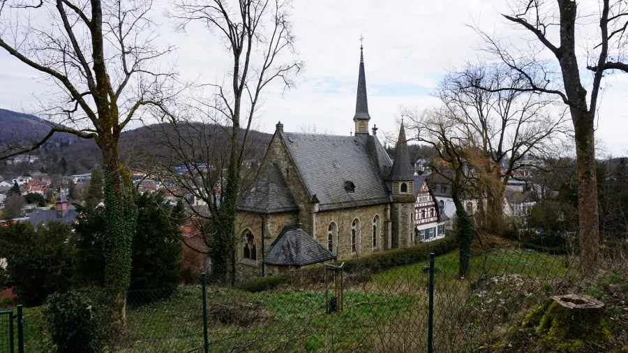 20230319_Deutschland_Hessen_3-Burgen-Weg (6) Stone church with a tall steeple on a hillside overlooking a town