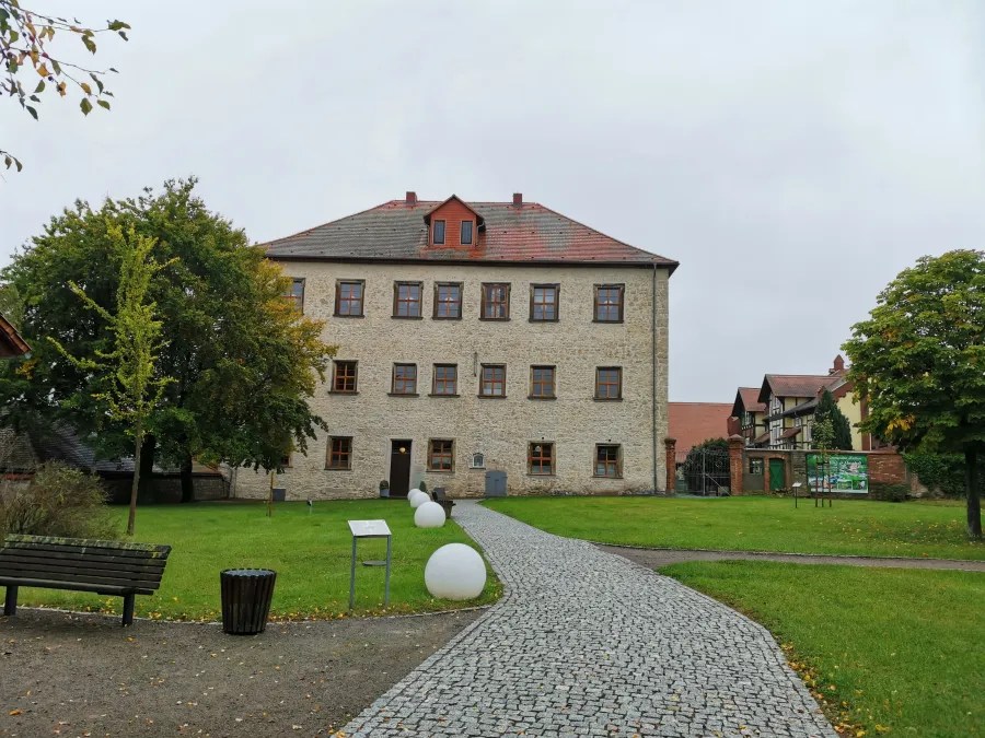A large, three-story stone building with a red roof and a cobblestone path across a courtyard.