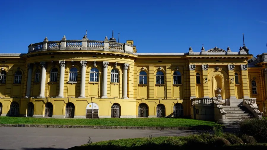 Yellow neoclassical building with white columns and arched windows under a bright blue sky