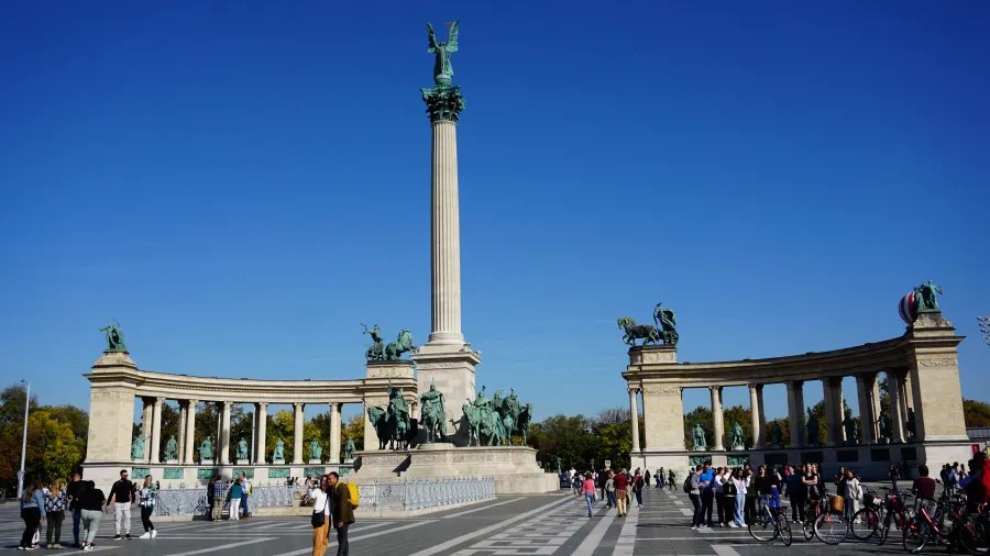 The Millennium Monument at Heroes' Square in Budapest with statues and people under a blue sky