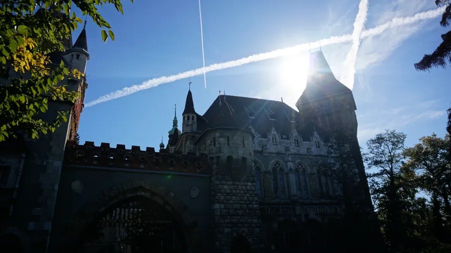 Vajdahunyad Castle in Budapest under a bright blue sky with airplane contrails