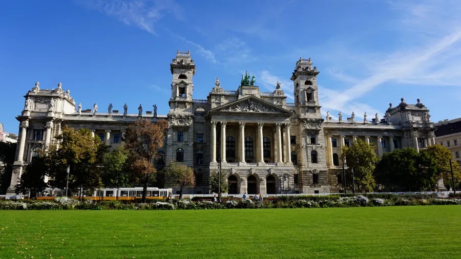 Ornate Neo-Renaissance building with statues and columns fronted by a green lawn