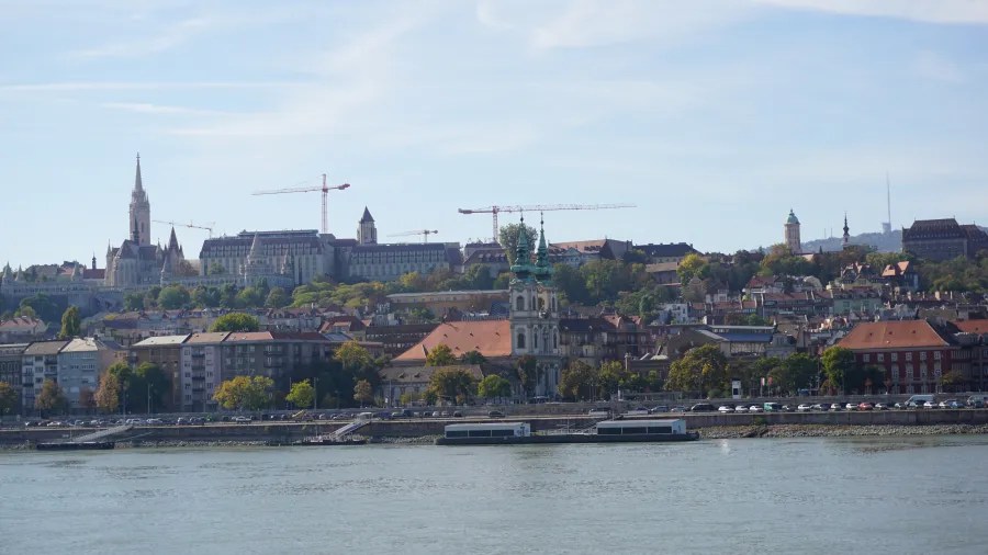 A view across a river of a historic city skyline with landmarks and construction cranes.