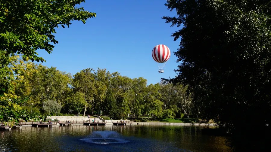 Red and white striped balloon flying above a park lake with a fountain.