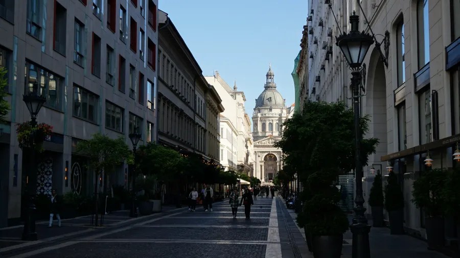 Pedestrians walking down a city street towards the domed St. Stephen's Basilica in Budapest.