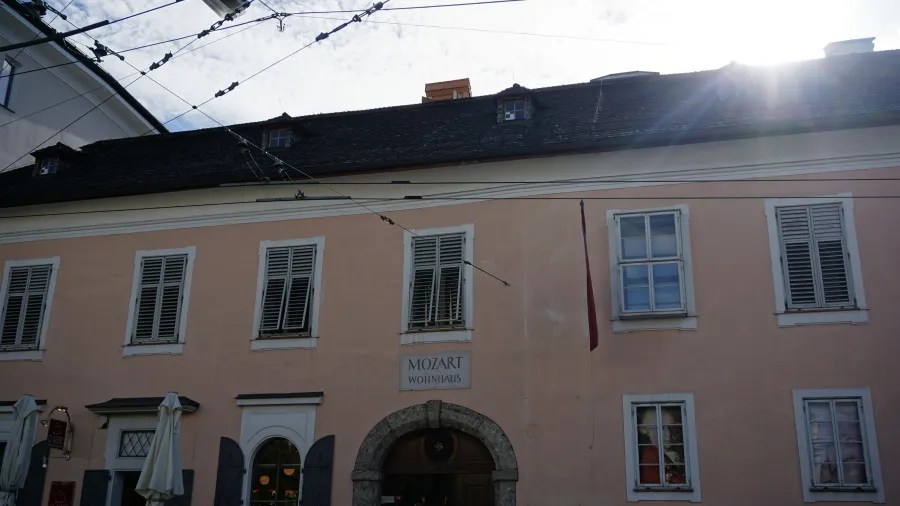 Pink building facade with shuttered windows and a sign above the archway reading MOZART WOHNHAUS.