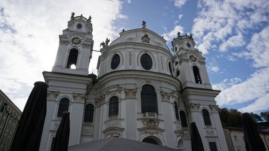 Ornate white Baroque cathedral with two clock towers under a partly cloudy sky