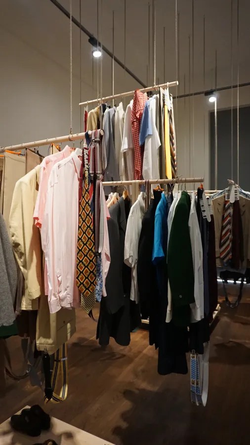 Clothing hanging from wooden rods suspended by ropes from the ceiling in a boutique display