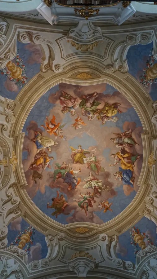 Ornate baroque ceiling fresco depicting allegorical figures among clouds and decorative stucco work