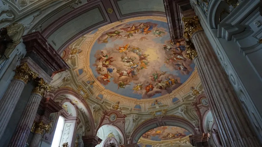 Ornate baroque church interior with a large fresco painting on the vaulted ceiling.