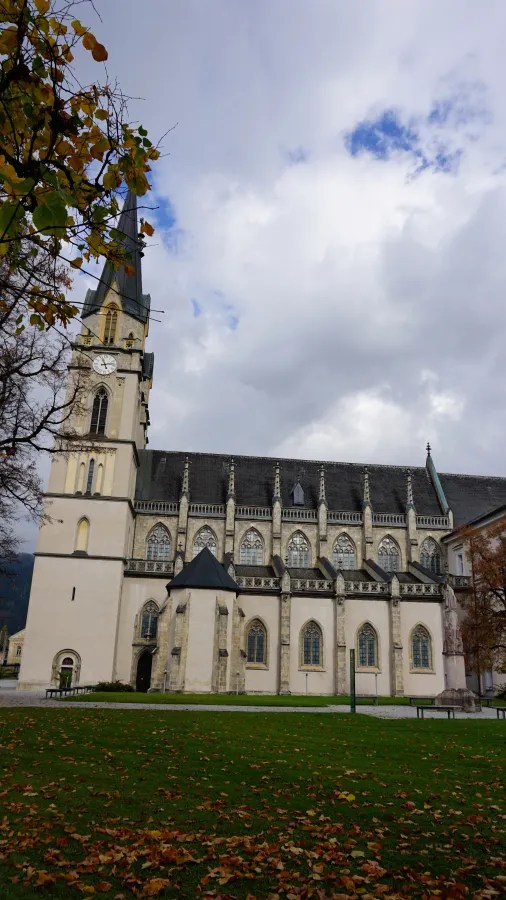 Gothic church with a tall clock tower overlooking a grassy lawn with autumn leaves.