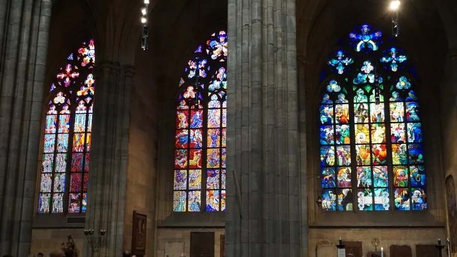 Three ornate stained-glass windows separated by large stone pillars inside a cathedral