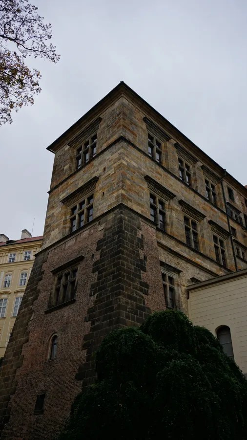A historic multi-story stone building with cross windows against a cloudy sky.
