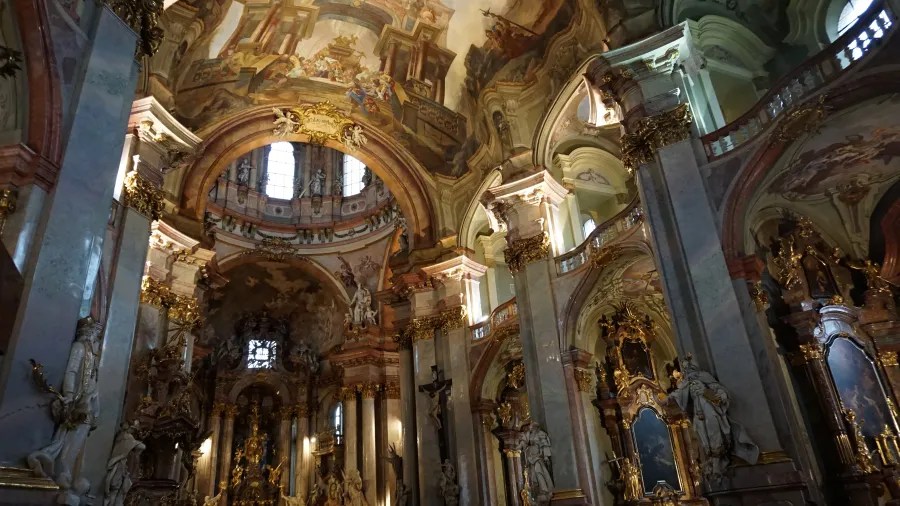 Ornate interior of a baroque church featuring elaborate ceiling frescoes and gilded statues.