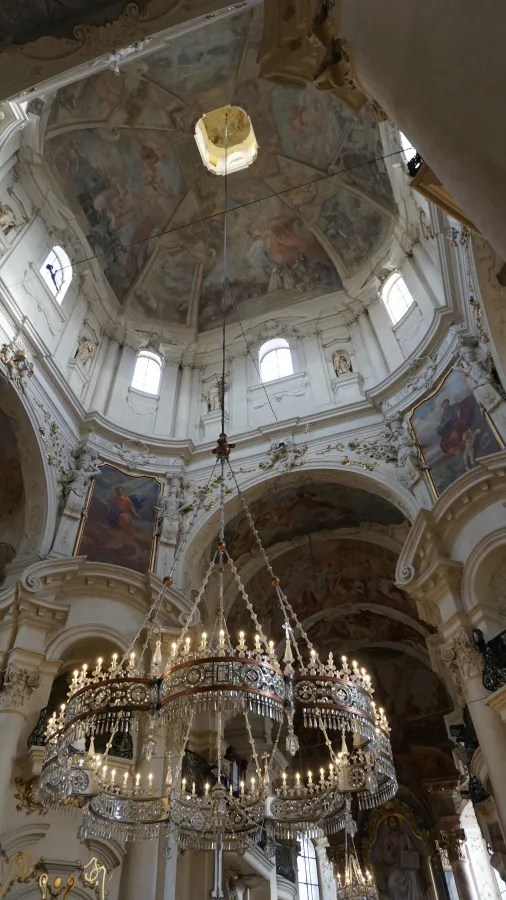 20221021_Tschechien_Prag (36) Large crystal chandelier hanging within an ornate church featuring a frescoed domed ceiling