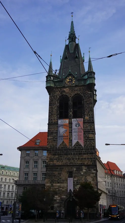 20221021_Tschechien_Prag (5) The stone Jindřišská Tower in Prague featuring a clock, green-tipped spire, and hanging banners.