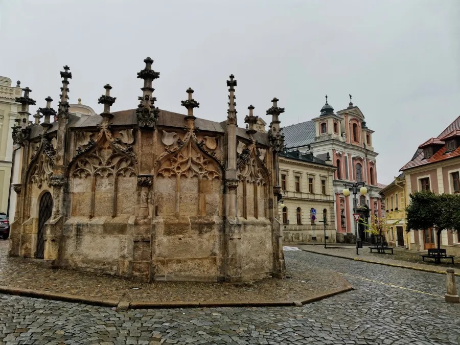 Ornate Gothic stone fountain in a cobblestone town square with historic buildings in the background