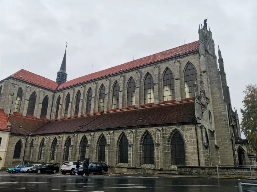 Large stone Gothic church featuring numerous pointed arch windows and a red tiled roof.