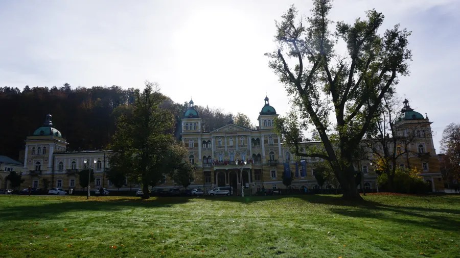 20221023_1_Tschechien_Marienbad (16) Grand yellow building with green domes situated behind a grassy lawn and trees.