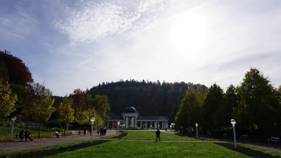 20221023_1_Tschechien_Marienbad (29) Sunny park landscape featuring a domed white colonnade and a forested hill.