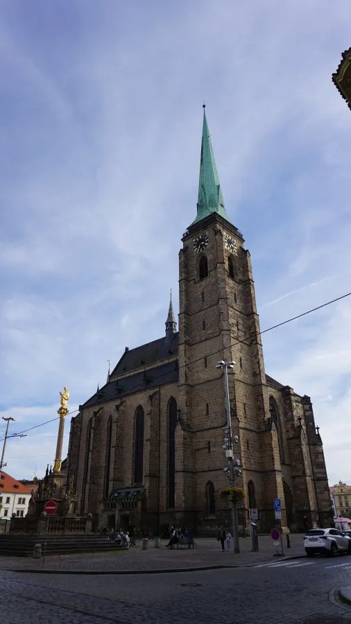 20221023_2_Tschechien_Pilsen (22) Large Gothic stone cathedral with a tall, pointed green spire and clock tower.