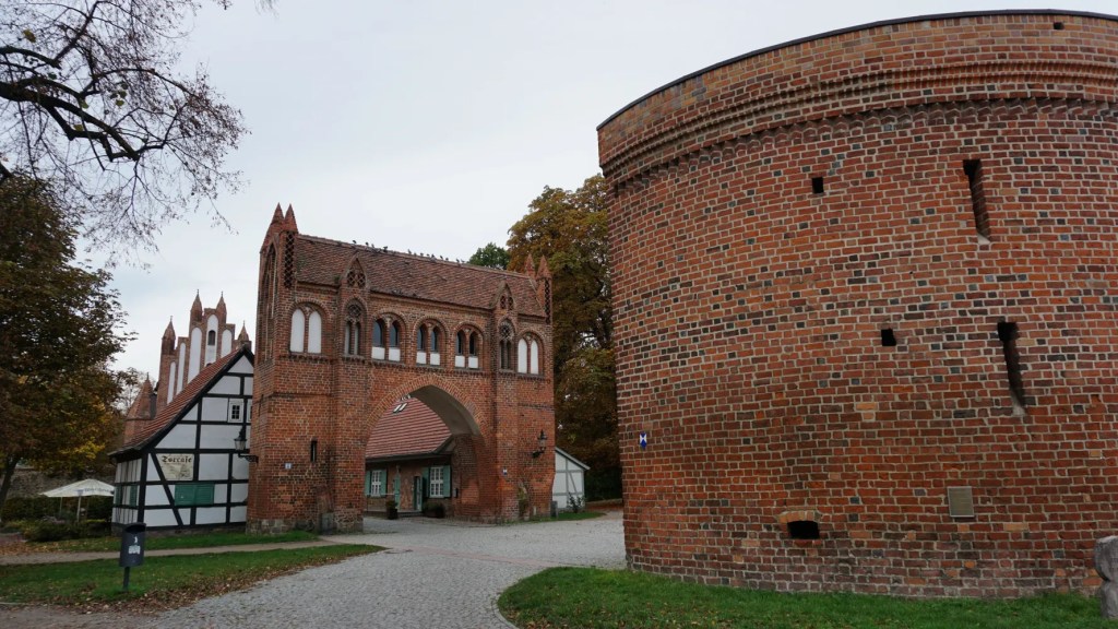 Historic red brick Gothic gate and round tower with a half-timbered building labeled Torcafé