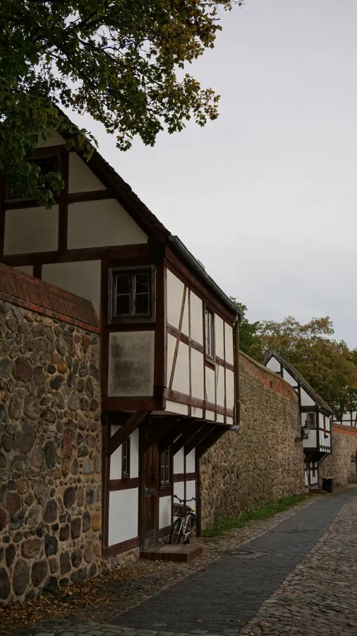 Half-timbered houses integrated into an ancient stone wall along a narrow paved lane