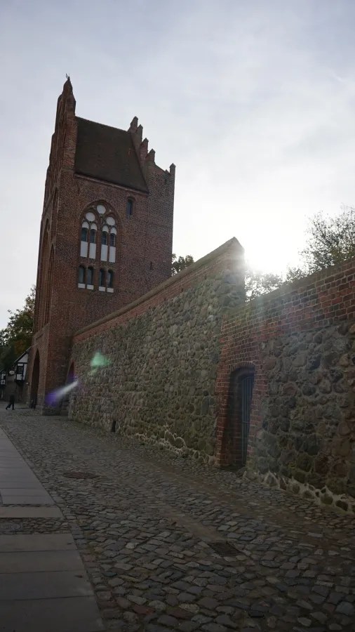 Historical red brick tower and stone wall along a cobblestone path