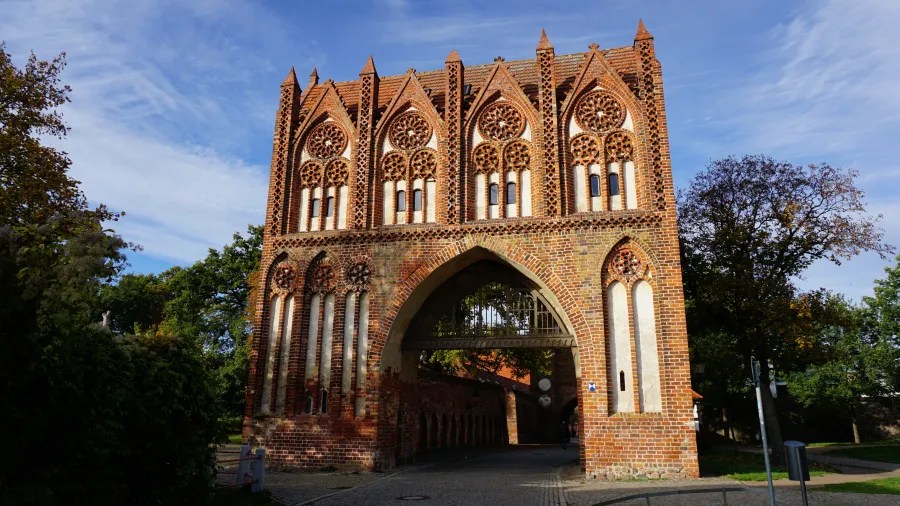 Ornate medieval Brick Gothic city gate with four decorative gables and a pointed archway.