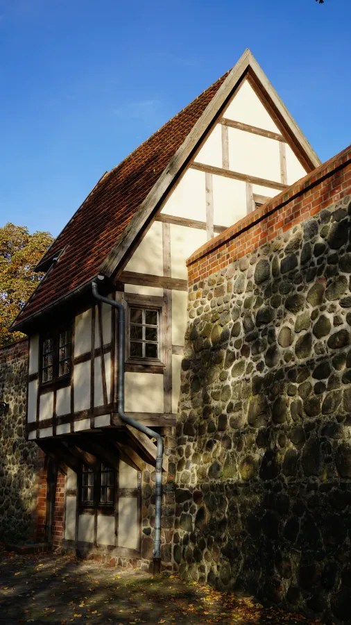 A traditional half-timbered house with a tiled roof behind a high stone wall.