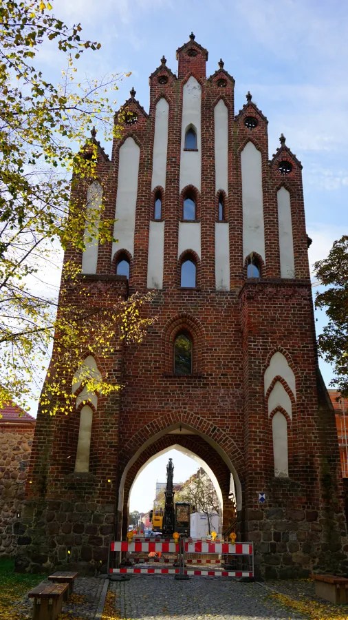 Historic red brick town gate with a stepped gable and large arched entrance.