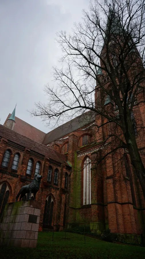 Red brick Gothic cathedral with a tall spire and a lion statue in the foreground