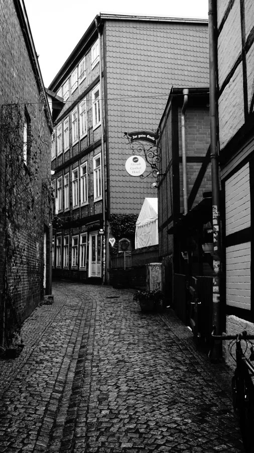 Black and white narrow cobblestone alley with signs for Zur guten Quelle and Altstadt Gasthof Hotel
