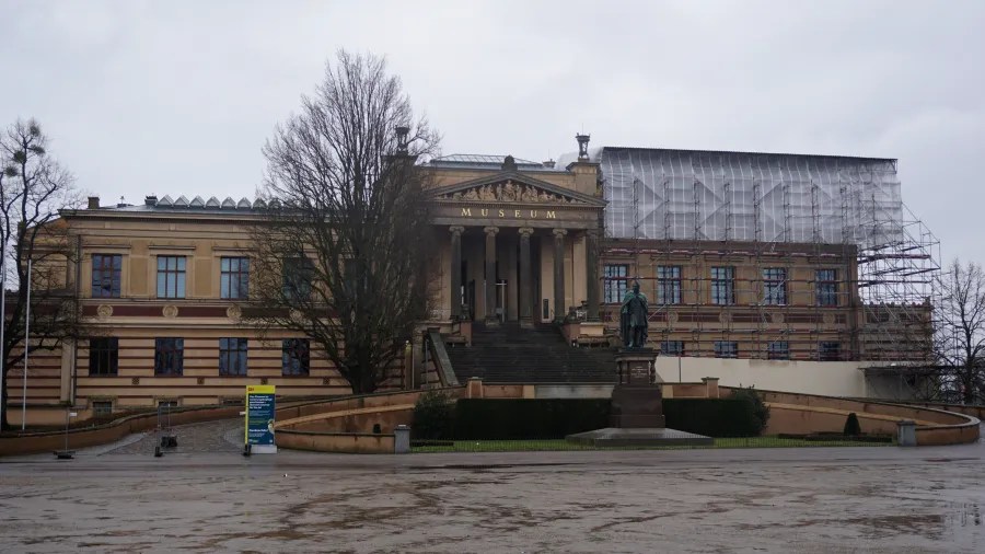 Classical museum building with 'MUSEUM' inscribed and construction scaffolding on one wing.