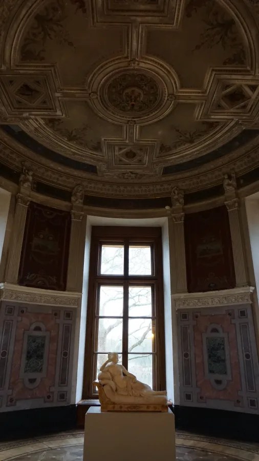 Reclining marble statue in an ornate room with a coffered ceiling and large window