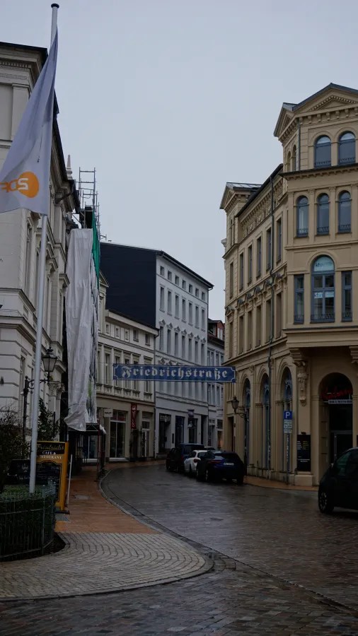 A wet city street with an overhead sign reading Friedrichstraße and a ZDF flag.