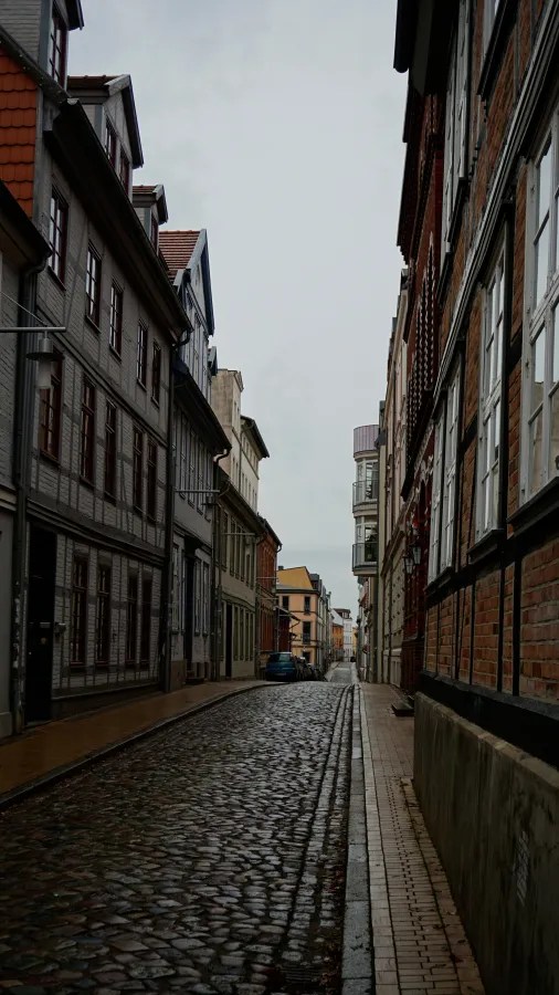 A narrow cobblestone street lined with historic half-timbered buildings under an overcast sky.