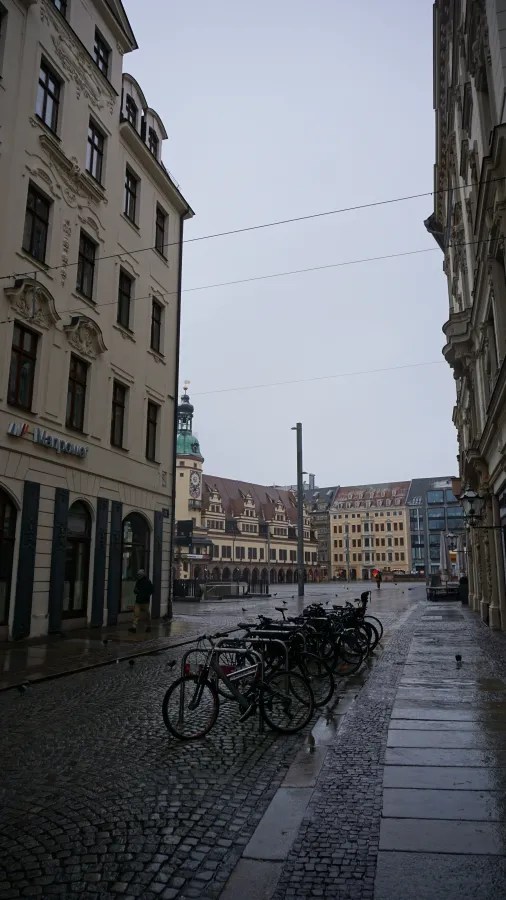 Parked bicycles on a wet cobblestone street with a Manpower sign leading to a historic square.