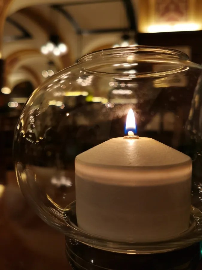 A lit white candle inside a clear glass globe in a dimly lit restaurant