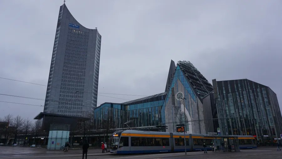 A yellow tram travels past the modern architectural landmarks of Augustusplatz in Leipzig.