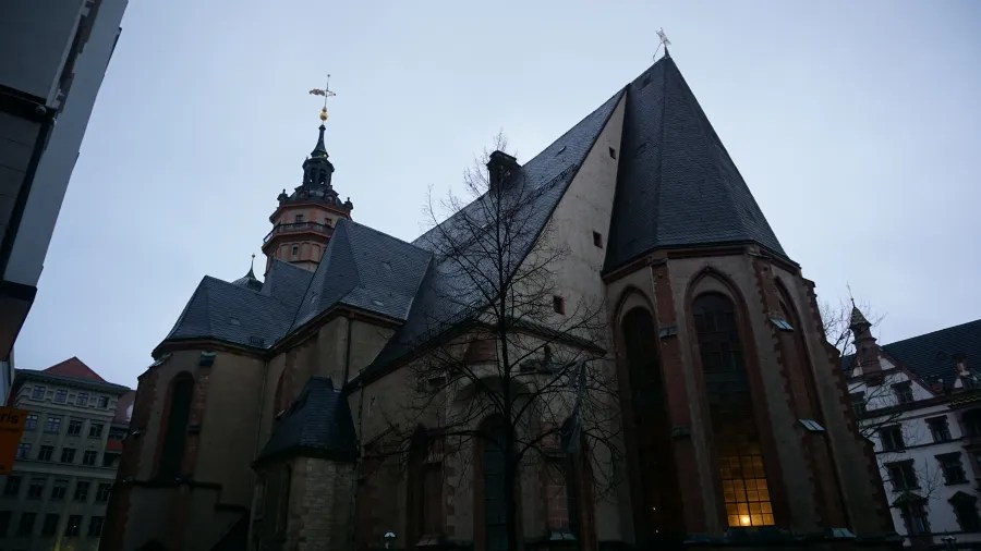 Gothic stone church with a tall spire and complex gabled roofs under an overcast sky