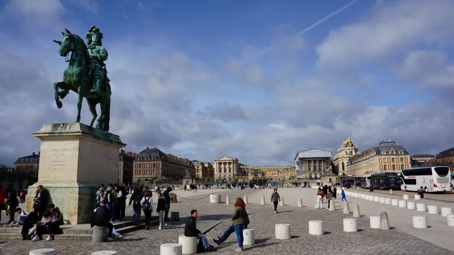 20230325_Frankreich_Paris (3) Crowd of people walking and sitting near equestrian statue in a large open square with historic buildings in the background under a partly cloudy sky