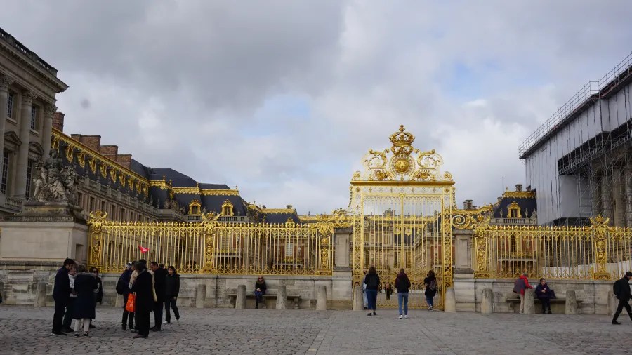 20230325_Frankreich_Paris (7) Visitors standing in front of ornate golden gates of a historic palace under a cloudy sky