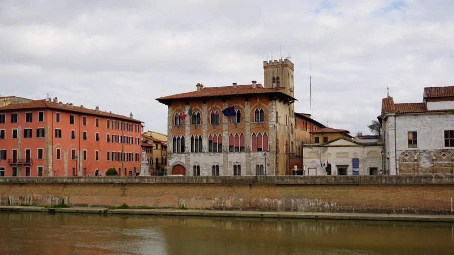 20230420_Italien_Toskana_Pisa (1) Historic buildings with arched windows along a river under a cloudy sky