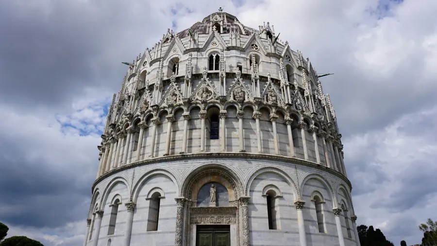 20230420_Italien_Toskana_Pisa (26) Exterior view of the ornate marble Baptistery of Pisa with detailed gothic architectural elements under a cloudy sky