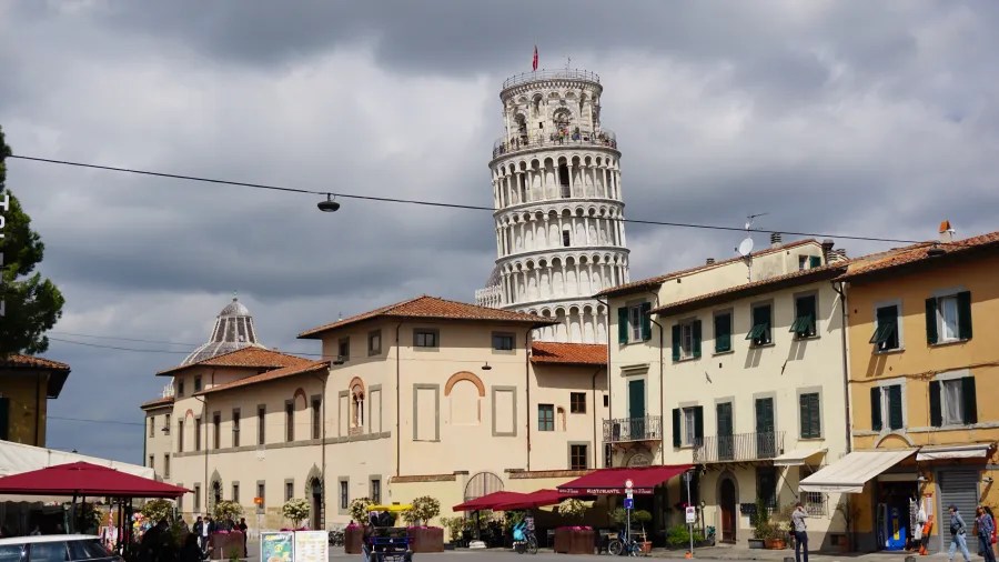 20230420_Italien_Toskana_Pisa (8) Leaning Tower of Pisa behind historic buildings under a cloudy sky in a busy square