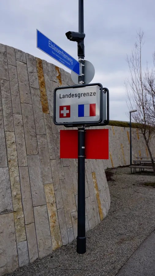 A signpost for Elsässerrheinweg and Landesgrenze with flags of Switzerland and France.