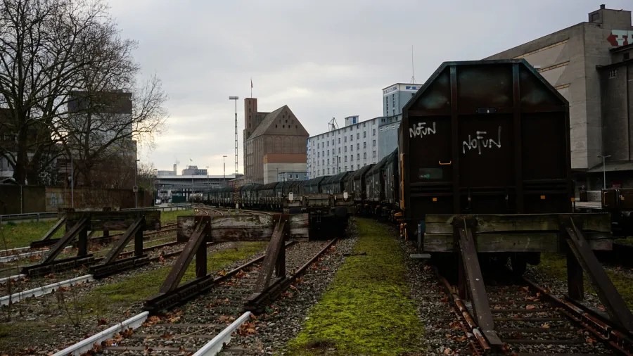 Freight train on tracks in an industrial area with 'NO FUN' graffiti on a car.