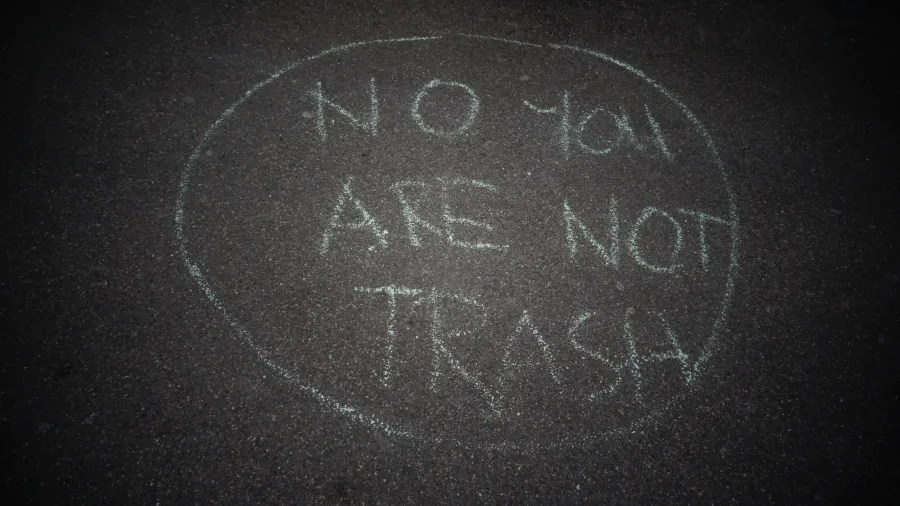Chalk message on asphalt inside a circle reading NO YOU ARE NOT TRASH